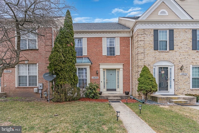 multi unit property with brick siding, a shingled roof, and a front lawn