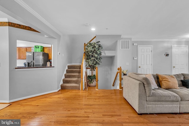 living room with stairway, baseboards, visible vents, ornamental molding, and light wood-type flooring