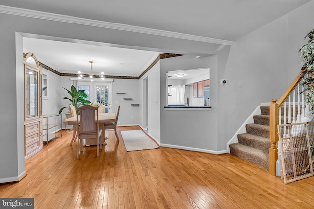 dining room with light wood-type flooring, baseboards, ornamental molding, and stairway