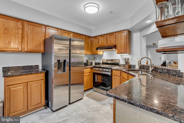 kitchen with brown cabinetry, dark stone counters, a sink, under cabinet range hood, and appliances with stainless steel finishes