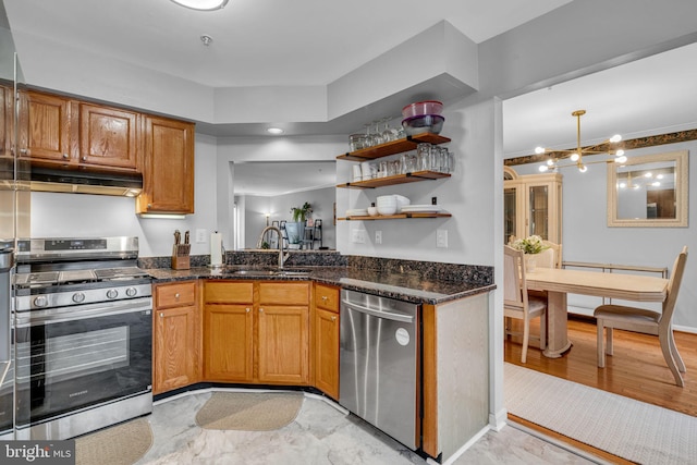 kitchen featuring under cabinet range hood, dark stone counters, appliances with stainless steel finishes, and a sink