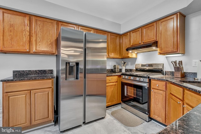 kitchen featuring under cabinet range hood, brown cabinetry, appliances with stainless steel finishes, and dark stone counters