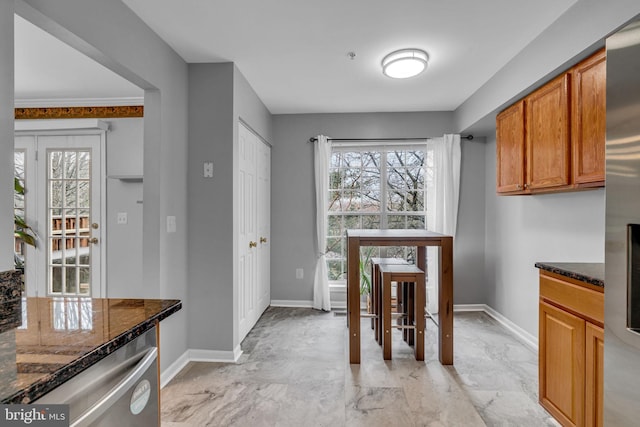 kitchen featuring baseboards, dark stone countertops, stainless steel fridge, brown cabinetry, and marble finish floor