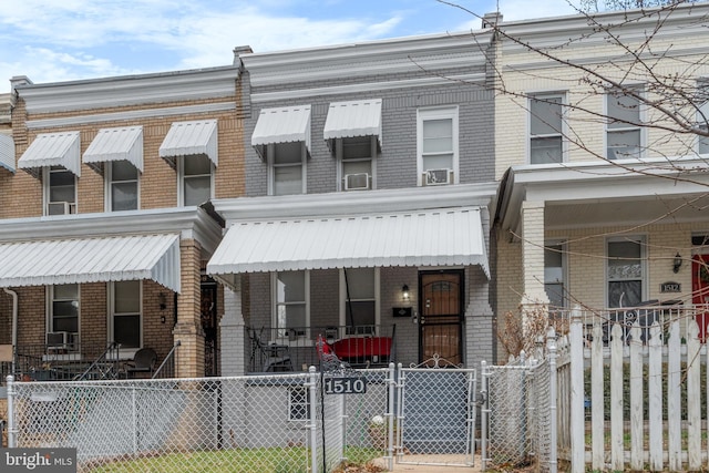 townhome / multi-family property with a gate, covered porch, brick siding, and a fenced front yard