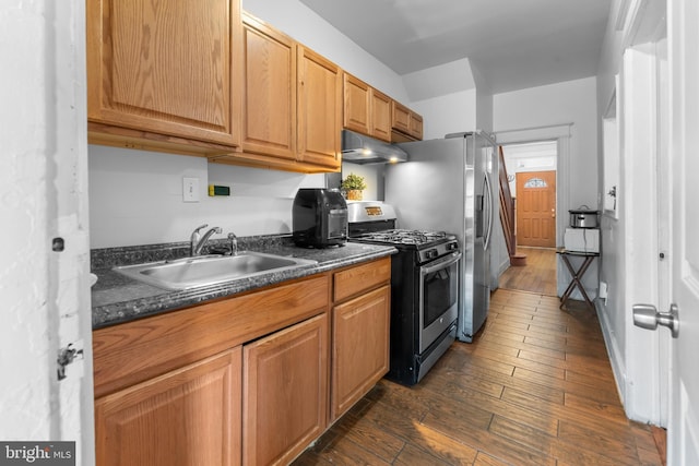 kitchen with dark countertops, under cabinet range hood, dark wood finished floors, gas stove, and a sink