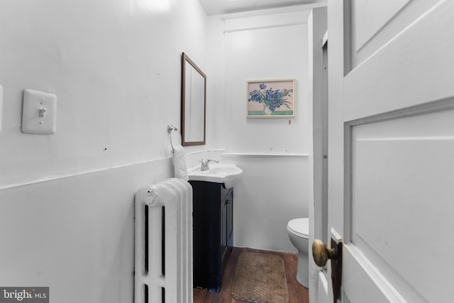 half bath with radiator, toilet, vanity, and wood finished floors