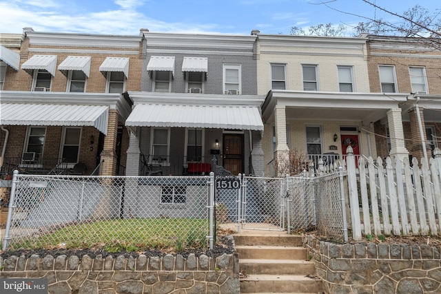 view of property featuring a fenced front yard, brick siding, a porch, and a gate