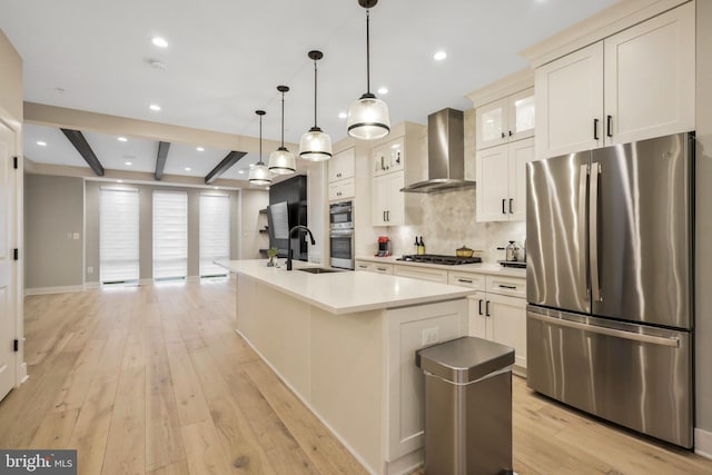 kitchen featuring light wood-type flooring, a sink, backsplash, appliances with stainless steel finishes, and wall chimney range hood