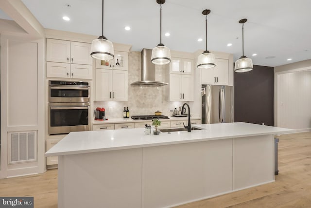 kitchen featuring visible vents, wall chimney range hood, light wood-style flooring, appliances with stainless steel finishes, and a sink