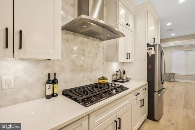 kitchen featuring black gas cooktop, white cabinets, freestanding refrigerator, and wall chimney range hood