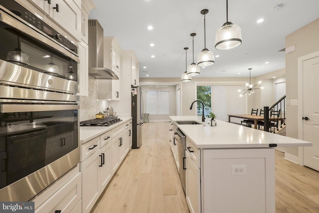 kitchen with stainless steel appliances, a sink, light countertops, wall chimney exhaust hood, and light wood-type flooring