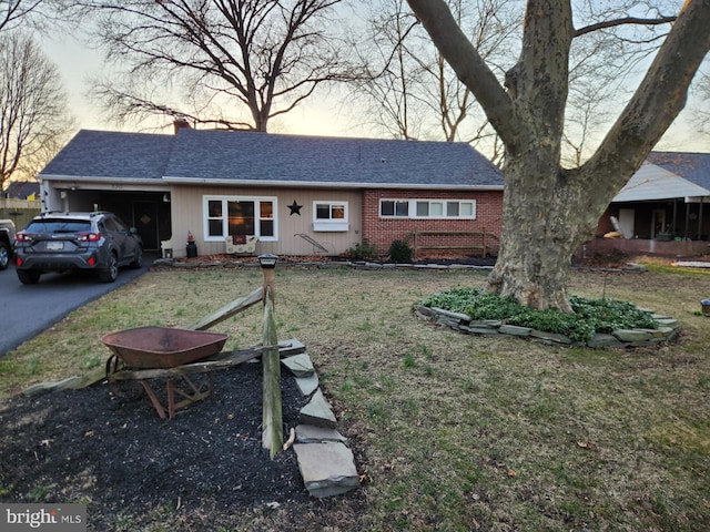 view of front facade featuring brick siding, a front lawn, a chimney, a garage, and driveway