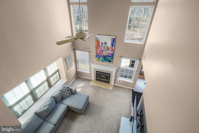 carpeted living area featuring a fireplace with flush hearth, a healthy amount of sunlight, a ceiling fan, and a towering ceiling