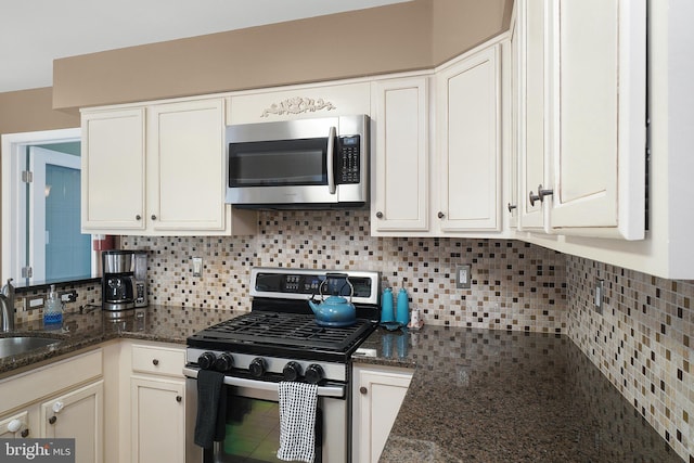 kitchen featuring a sink, backsplash, white cabinetry, stainless steel appliances, and dark stone counters