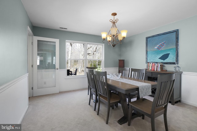 dining room featuring a wainscoted wall, an inviting chandelier, visible vents, and light carpet