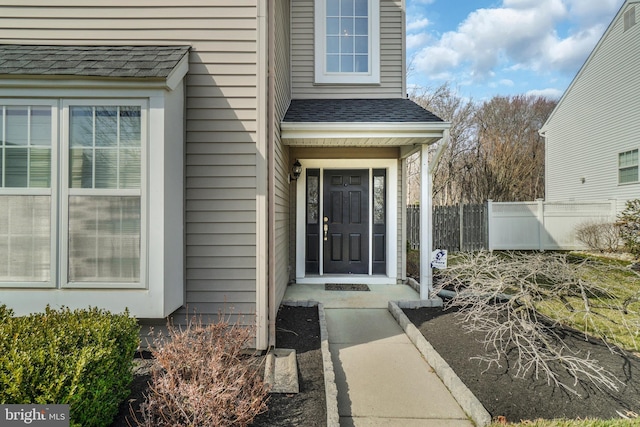 property entrance featuring roof with shingles and fence