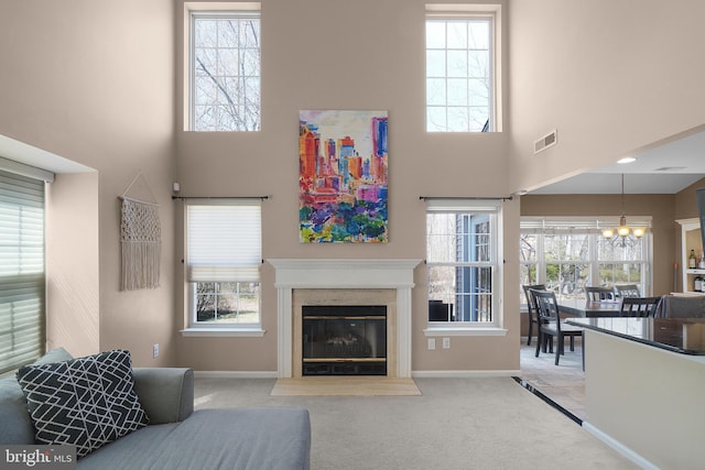 living area featuring visible vents, a fireplace with flush hearth, an inviting chandelier, carpet flooring, and baseboards