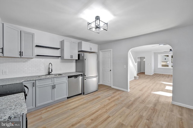 kitchen with tasteful backsplash, a sink, appliances with stainless steel finishes, arched walkways, and open shelves