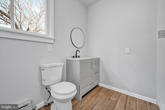 bathroom featuring toilet, a baseboard heating unit, wood finished floors, baseboards, and vanity