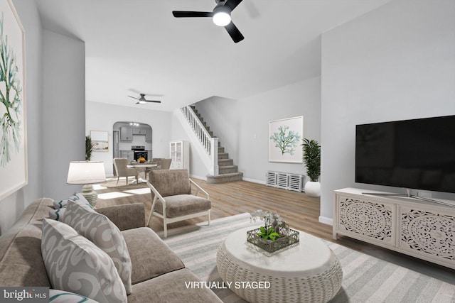 living room with a ceiling fan, wood finished floors, arched walkways, baseboards, and stairs