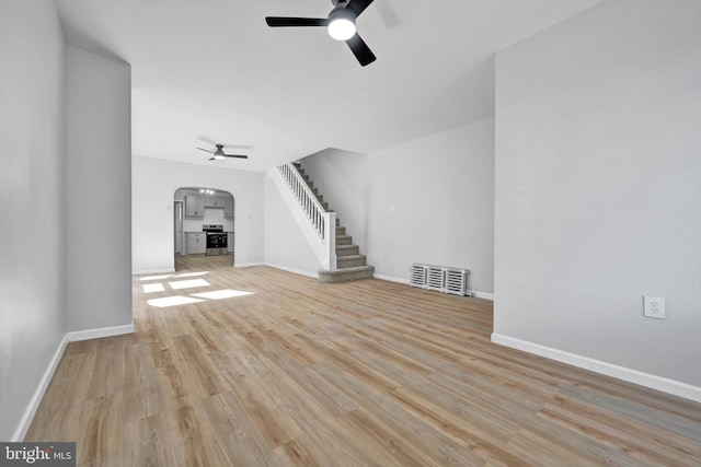 unfurnished living room with ceiling fan, baseboards, stairway, wood finished floors, and arched walkways