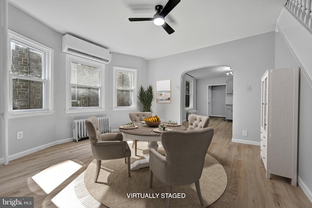 dining room with light wood-type flooring, arched walkways, radiator heating unit, and a wall mounted AC