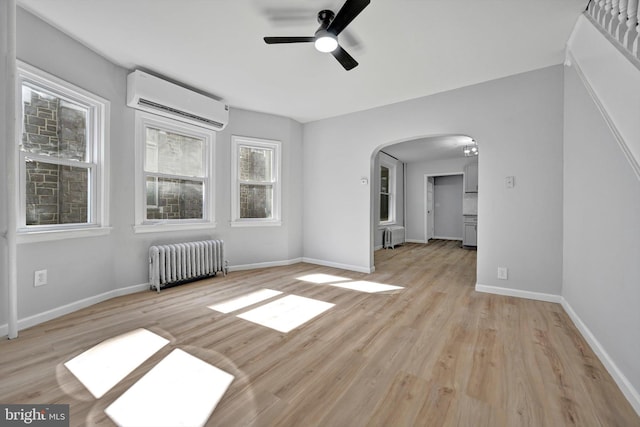 spare room featuring light wood-style flooring, radiator heating unit, arched walkways, and a wall mounted AC