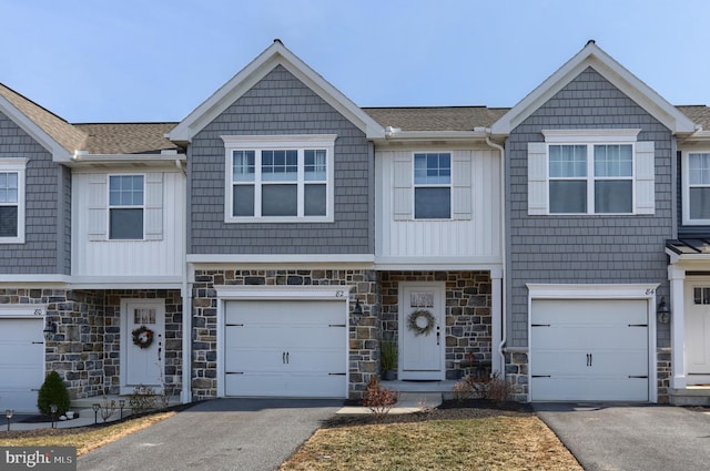 multi unit property featuring aphalt driveway, stone siding, and roof with shingles