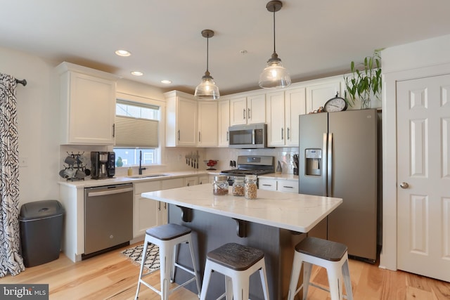 kitchen featuring light wood-type flooring, a sink, white cabinetry, appliances with stainless steel finishes, and a breakfast bar area