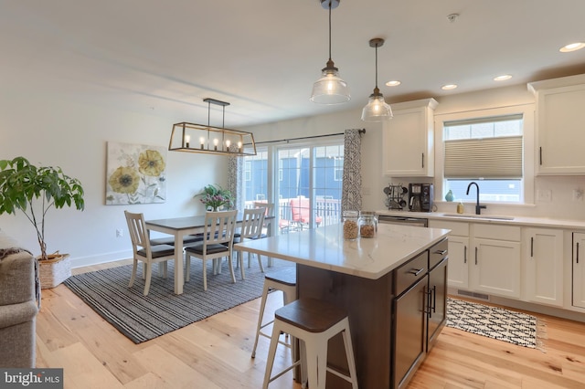 kitchen featuring white cabinets, a kitchen island, light wood-style floors, and a sink