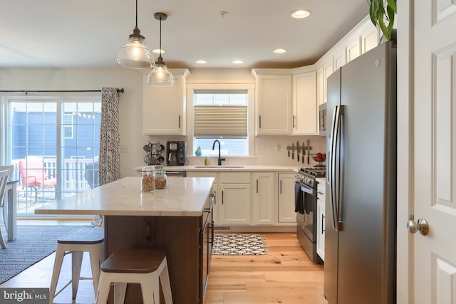 kitchen with a breakfast bar, a sink, a kitchen island, white cabinetry, and stainless steel appliances