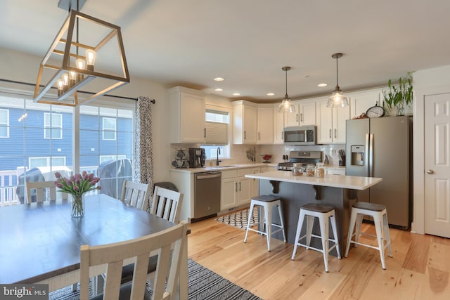 kitchen featuring stainless steel appliances, light wood finished floors, plenty of natural light, and white cabinetry