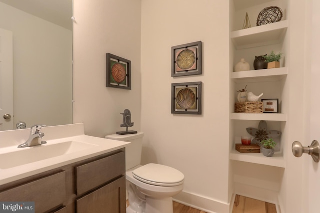 bathroom featuring vanity, built in shelves, wood finished floors, baseboards, and toilet