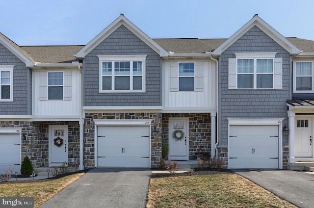 townhome / multi-family property with stone siding, driveway, an attached garage, and roof with shingles