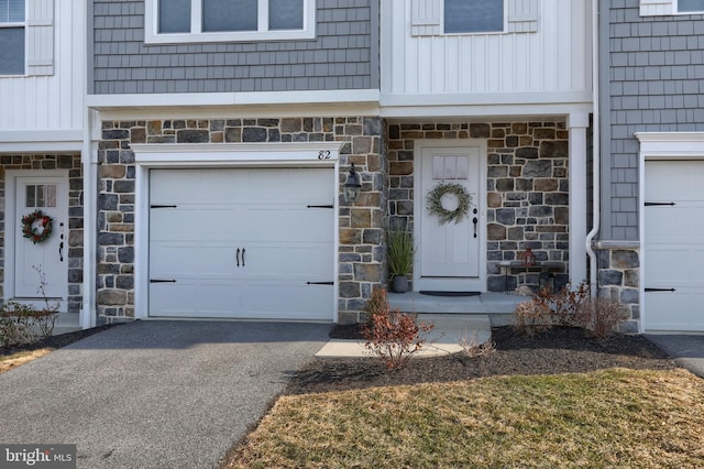 property entrance featuring stone siding, driveway, and an attached garage