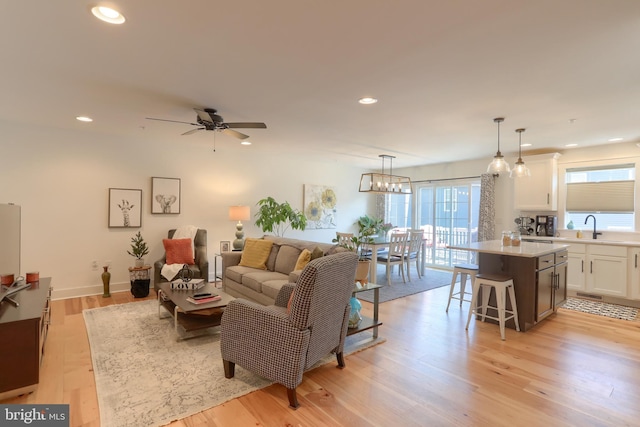 living area with baseboards, recessed lighting, ceiling fan with notable chandelier, and light wood-style floors