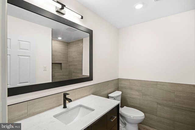 bathroom featuring toilet, vanity, recessed lighting, wainscoting, and tile walls