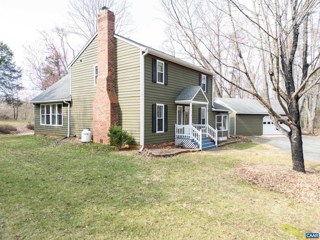 view of front of house featuring an outbuilding, a chimney, a front lawn, a garage, and aphalt driveway