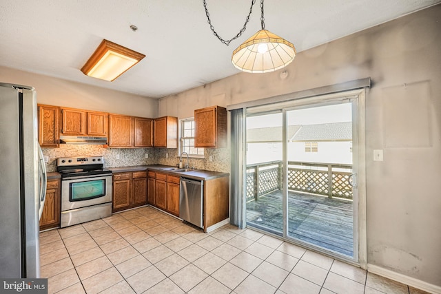 kitchen with brown cabinets, a sink, under cabinet range hood, stainless steel appliances, and decorative backsplash