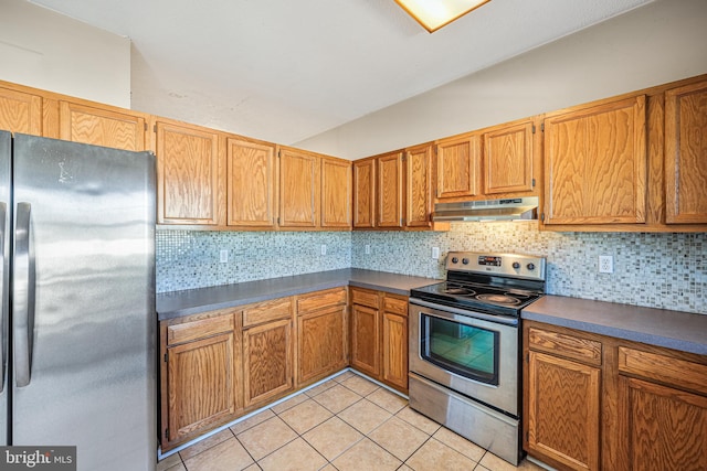 kitchen featuring under cabinet range hood, backsplash, dark countertops, stainless steel appliances, and light tile patterned floors