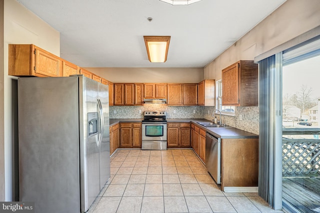 kitchen with backsplash, light tile patterned floors, brown cabinets, appliances with stainless steel finishes, and a sink