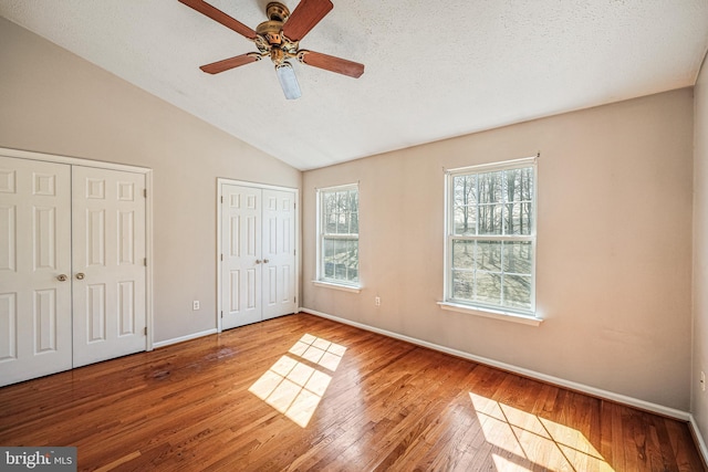 unfurnished bedroom with baseboards, multiple closets, lofted ceiling, hardwood / wood-style flooring, and a textured ceiling