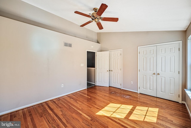 unfurnished bedroom with wood finished floors, visible vents, baseboards, lofted ceiling, and two closets