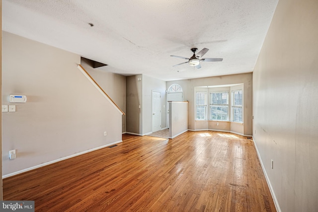 unfurnished living room with hardwood / wood-style flooring, a ceiling fan, baseboards, and a textured ceiling