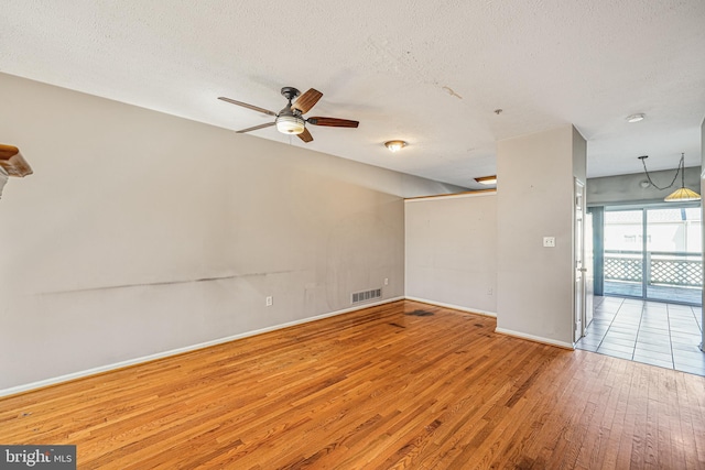 unfurnished room with ceiling fan, wood finished floors, visible vents, and a textured ceiling