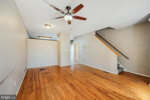 unfurnished living room with visible vents, baseboards, stairway, wood finished floors, and a ceiling fan