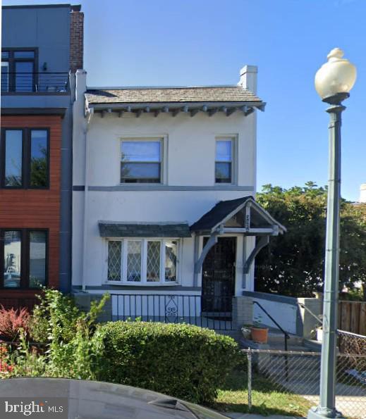 view of front facade featuring stucco siding, a chimney, and fence