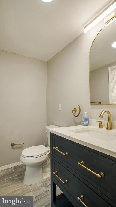 half bathroom featuring vanity, toilet, baseboards, and wood finish floors