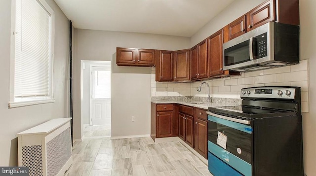 kitchen with a sink, backsplash, radiator heating unit, appliances with stainless steel finishes, and brown cabinetry