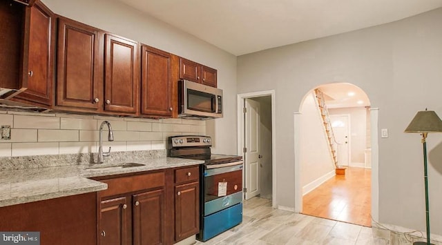 kitchen featuring backsplash, light stone countertops, arched walkways, stainless steel appliances, and a sink